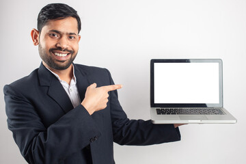 smiling indian suit man holding laptop and pointing finger towards empty laptop screen for advertisement