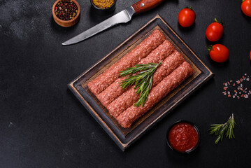 Fresh raw mince for grilled kebab with spices and herbs on a dark concrete background