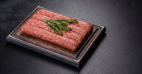 Fresh raw mince for grilled kebab with spices and herbs on a dark concrete background