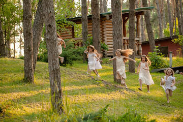 Group of happy preteen girls running among trees on green lawn in country estate