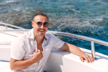 Portrait of adult man sitting on a yacht and looking at camera and wearing white shirt. Relaxing in summer during the trip. 