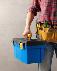 Worker man holding construction toolbox near concrete or cement wall. Male hand and tool box - 494296188