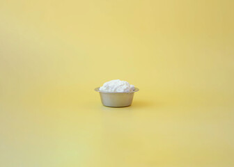 A small iron bowl for dogs filled with cottage cheese stands on a yellow background the concept of natural nutrition
