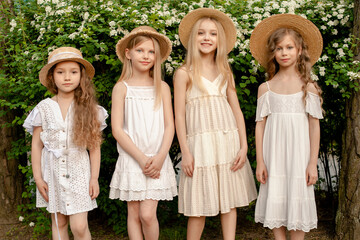 Smiling tween girls standing in summer park near green blooming bush