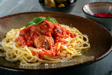 The classic spaghetti pasta with meatballs is served on a brown plate. Italian dish with meat, tomato bolognese sauce and pasta, closeup