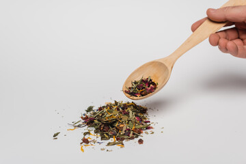 Cropped view of man holding wooden spoon with dry tea on white background.