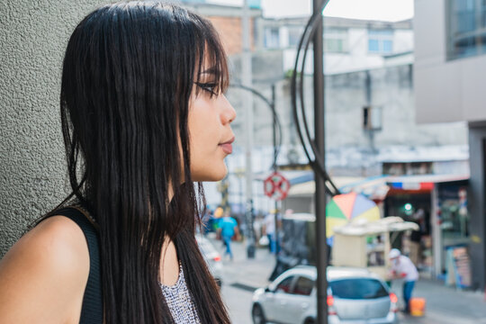beautiful brown-skinned latina woman, standing next to a concrete wall waiting for another person while watching people pass by on the street. concept of freedom