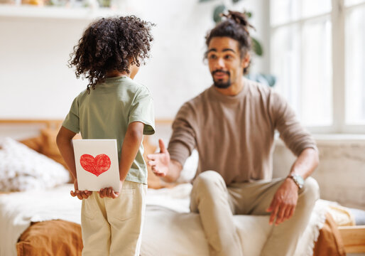 Little child making surprise for daddy on fathers day, giving handmade postcard for birthday to dad