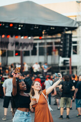 Friends taking selfie with a smartphone and drinking beer on a music festival