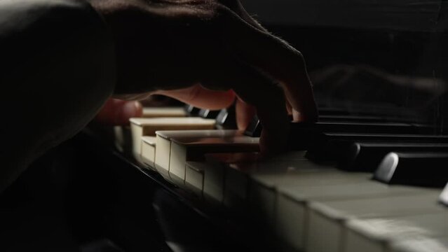 Male pianist plays fast music on piano in dark. Musician touches white and black keys of string instrument with his fingers creating musical melody. Male hands close up. Slow motion ready at 59.94fps.