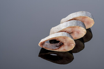 pieces of salted herring fish on a mirror background