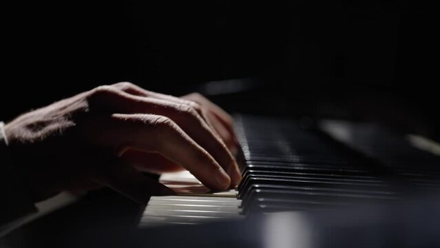 Male hands touch piano keys and play fast jazz melody. Pianist plays chords creating music on piano in dark. Keys of musical instrument. Musician's fingers close up. Slow motion ready at 59.94fps.