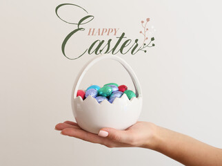 Easter greeting card with female hand holding basket of chocolate eggs
