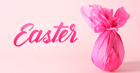 Chocolate egg wrapped in pink paper and text EASTER on color background