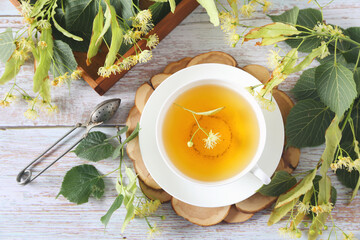 Cup of herbal linden tea with linden flowers on light background