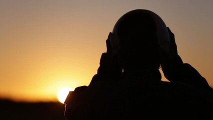 Military Fighter Pilot putting on his Pilot Helmet during Sunset in the Air Base.  