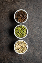 Three different types of pepper spice. Green, white and black peppercorn in bowls.