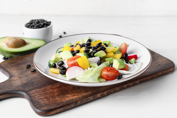 Board with plate of Mexican vegetable salad on light wooden table, closeup