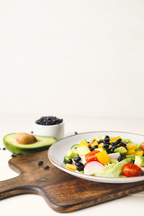 Board with plate of Mexican vegetable salad on light wooden table