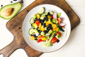 Board with plate of Mexican vegetable salad on light wooden background, closeup