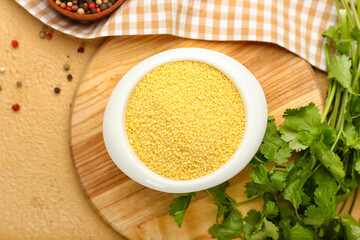 Bowl of raw couscous with parsley on color background