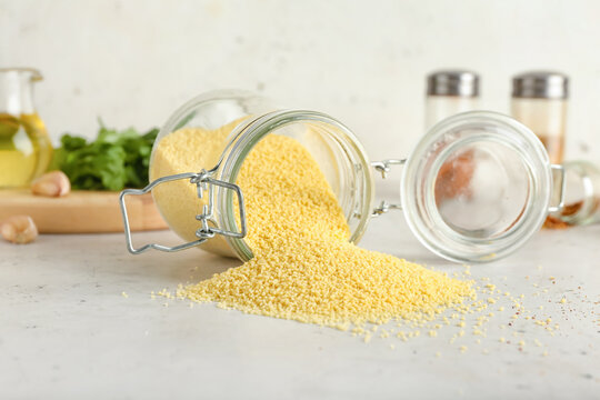 Jar with raw couscous on light background