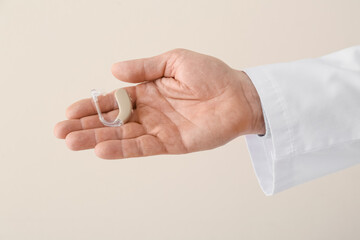 Hand of doctor with hearing aid on light background