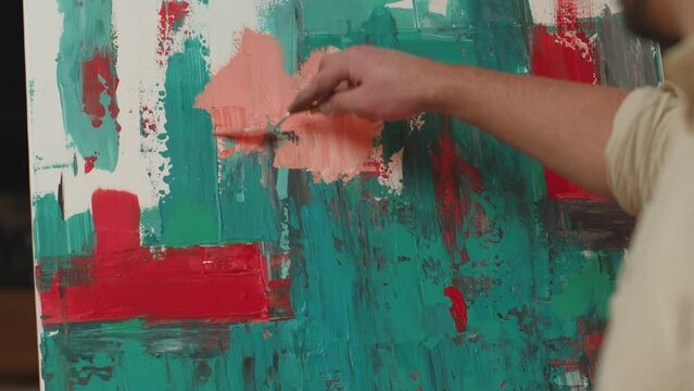 Artist guy painting picture on canvas with artistic tool, putting paints strokes, close-up. Prores codec. Handheld video