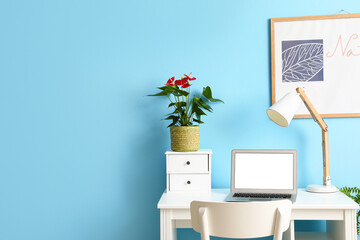 Workplace with modern laptop, lamp and Anthurium flower near color wall