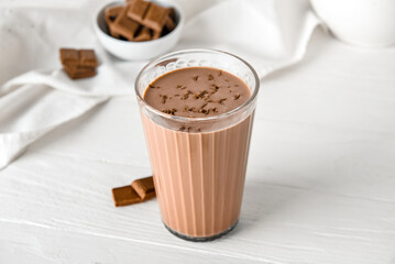 Glass of delicious chocolate milk on white wooden background