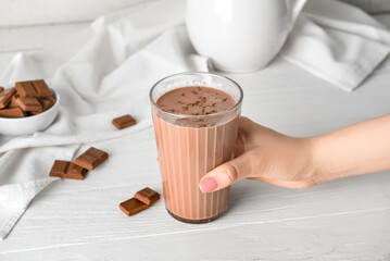 Female hand holding glass of delicious chocolate milk on white wooden background