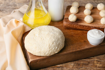 Board with dough for preparing lazy dumplings and sour cream on wooden background, closeup