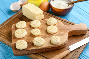 Board with raw lazy dumplings and butter on color wooden background, closeup