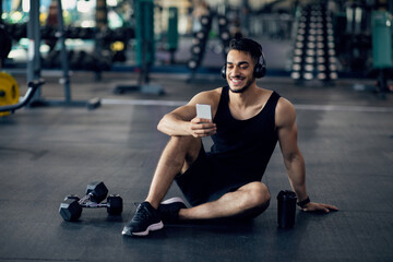Fototapeta na wymiar Fitness Application. Smiling Middle Eastern Sportsman Using Smartphone At Gym