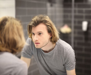 Fototapeta premium young man looking in the mirror,combing his hair,looking at problems on face.