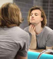 young man looking in the mirror,combing his hair,looking at problems on face.