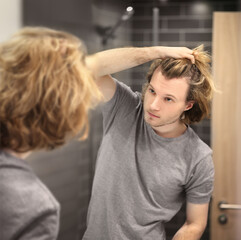 Fototapeta premium young man looking in the mirror,combing his hair,looking at problems on face.