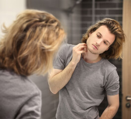 young man looking in the mirror,combing his hair,looking at problems on face.