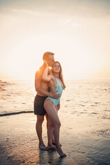 A loving couple walks along the beach by the sea. Young family at sunset by the Mediterranean Sea. Vacation concept. A woman in a swimsuit and a man in shorts at sunset by the sea. Selective focus.