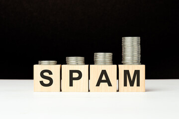 there are four wooden cubes with letters on the white table. spam word. black background with increasing stack of coins on cubes.