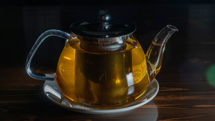 Glass teapot with tea on dark background. Green tea and teapot on wooden table. Advertising composition.