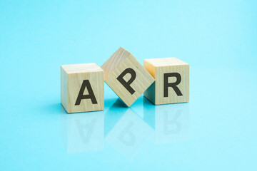 three wooden cubes with the letters APR on the bright surface of a blue table