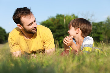 Little boy with rugby ball and his father lying on green grass in park