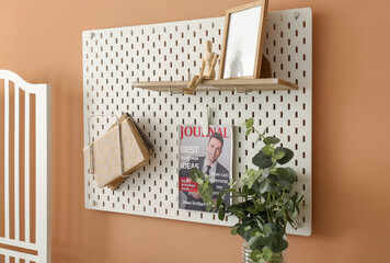 Pegboard with magazine, books, mannequin and frame hanging on beige wall