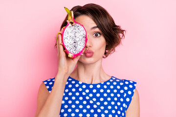 Photo of flirty young brunette lady show dragon fruit blow kiss wear dotted blouse isolated on pink color background