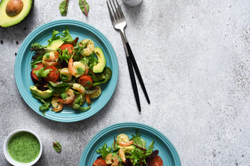 Green mix salad with tomatoes and shrimp and sauce on a concrete background. View from above