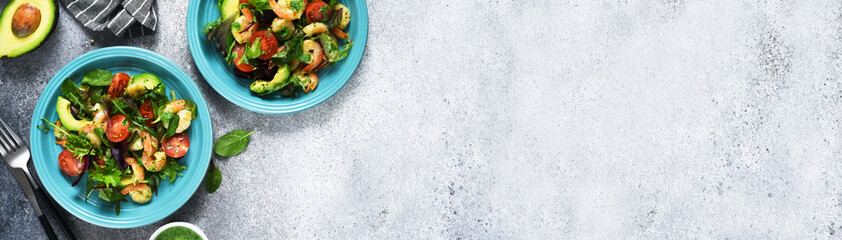 Green mix salad with tomatoes and shrimp and sauce on a concrete background. View from above