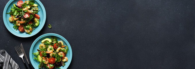 Fototapeta premium Mix salad with tomatoes and shrimp with pesto sauce on a black background. View from above