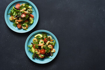Mix salad with tomatoes and shrimp with pesto sauce on a black background. View from above
