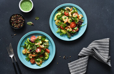 Mix salad with tomatoes and shrimp with pesto sauce on a black background. View from above